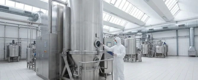 Technician inspecting a large stainless steel pharmaceutical dryer in a clean industrial processing facility.